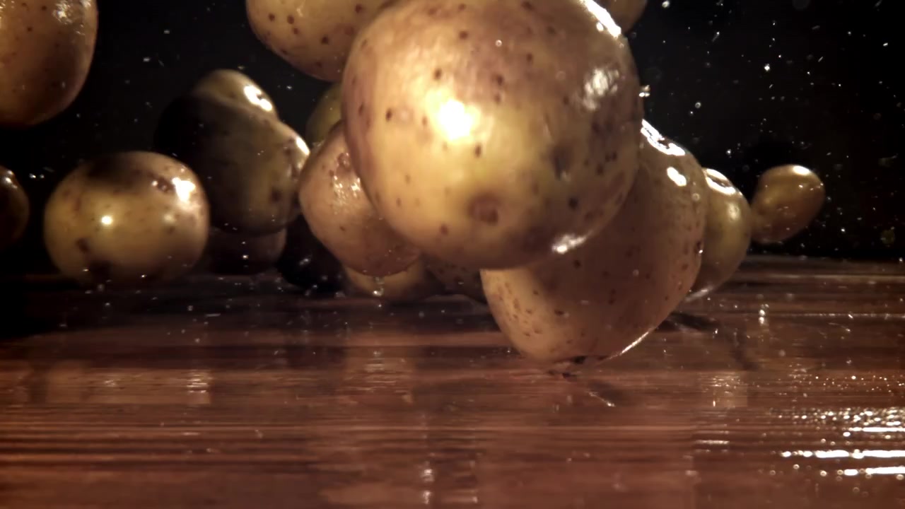 Patate fresche che cadono e schizzano acqua su una superficie di legno al rallentatore