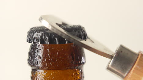 Fresh-wet-beer-bottle-cap-with-water-drops-is-opend-by-a-wooden-bottle-opener-in-slow-motion-on-white-background