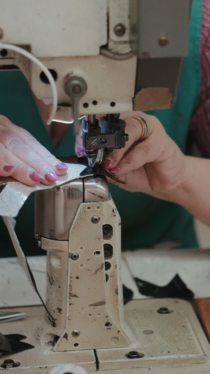 Vertical closeup of worker stitching leather material in footwear production