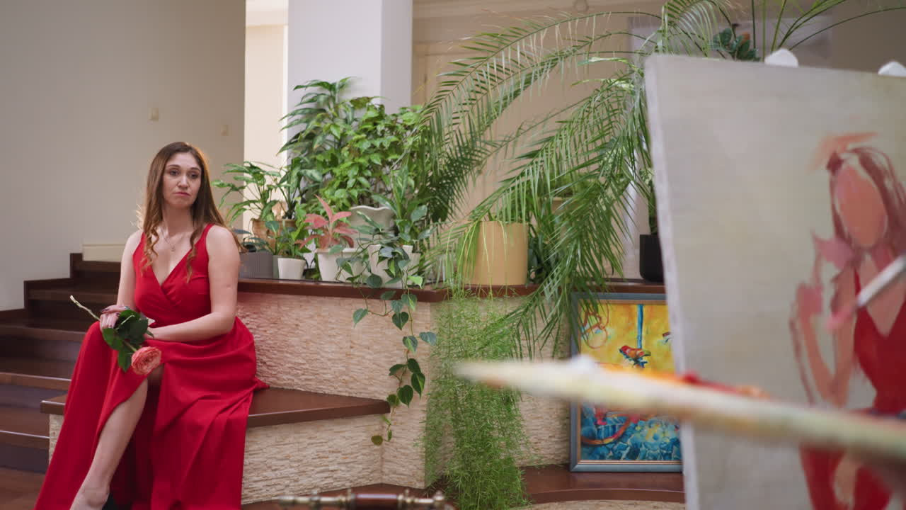 грустная женщина с розой позирует для художника в галерее. соблазнительная леди в красном платье сидит, в то время как художник смешивает оттенки на борту на живом рисунке.