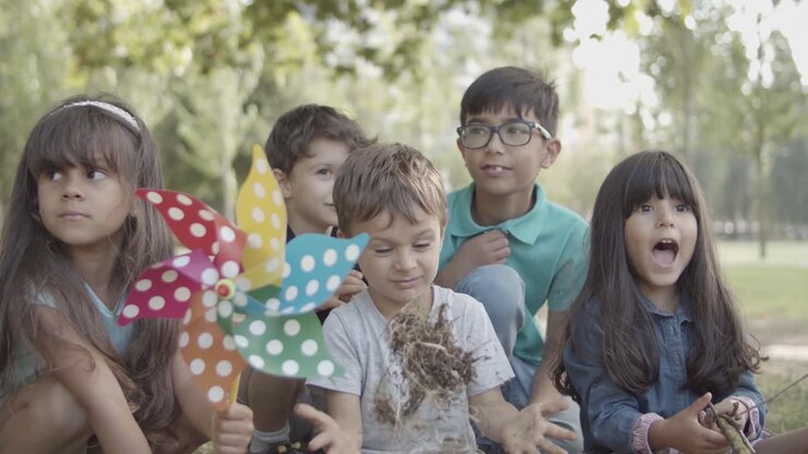 Gruppo di bambini multietnici seduti insieme al parco per una lezione all'aperto.