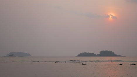 hazy red sunset behind small clouds over ocean and hills