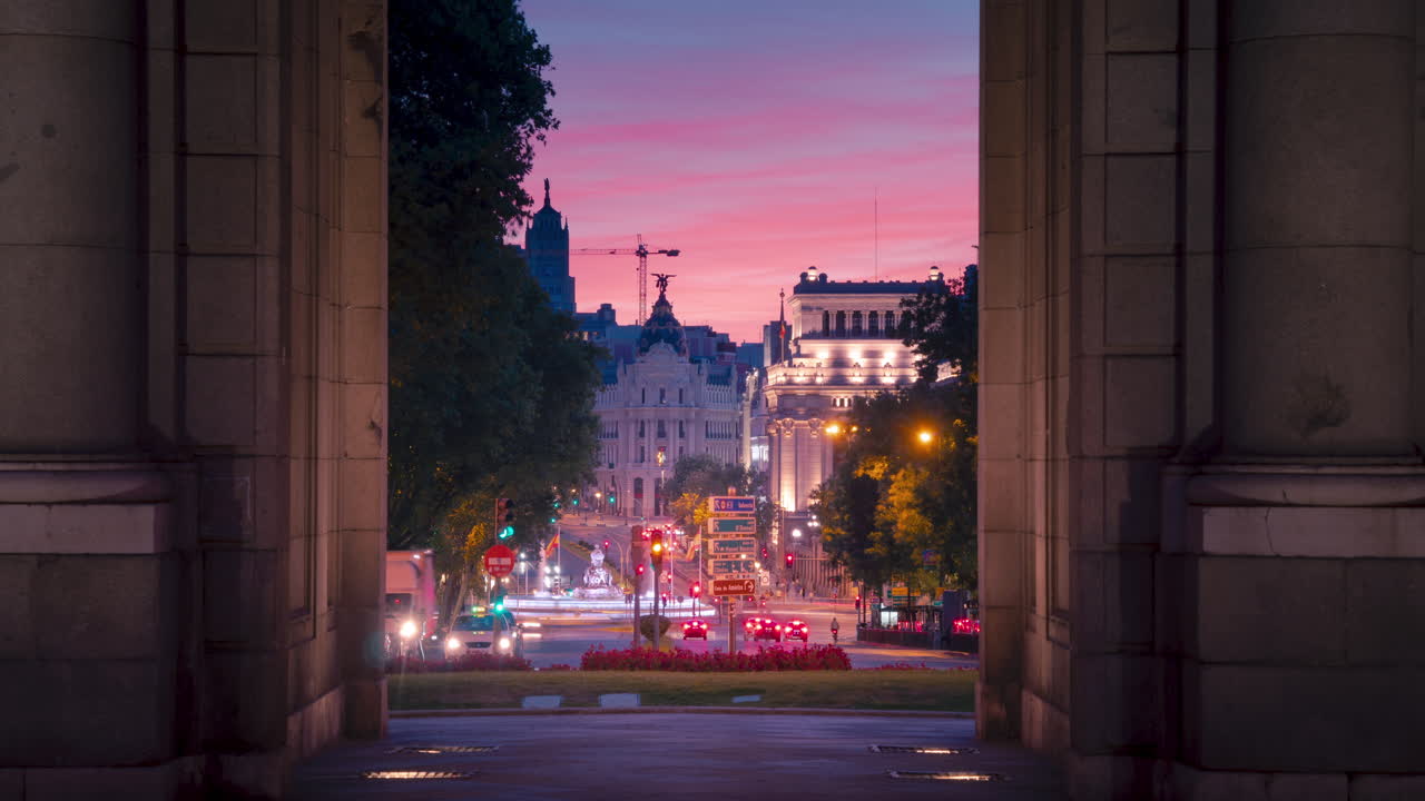 lapso de tiempo durante la puesta de sol del edificio metrópolis y cibeles visto a través del monumento puerta de alcala en madrid, españa