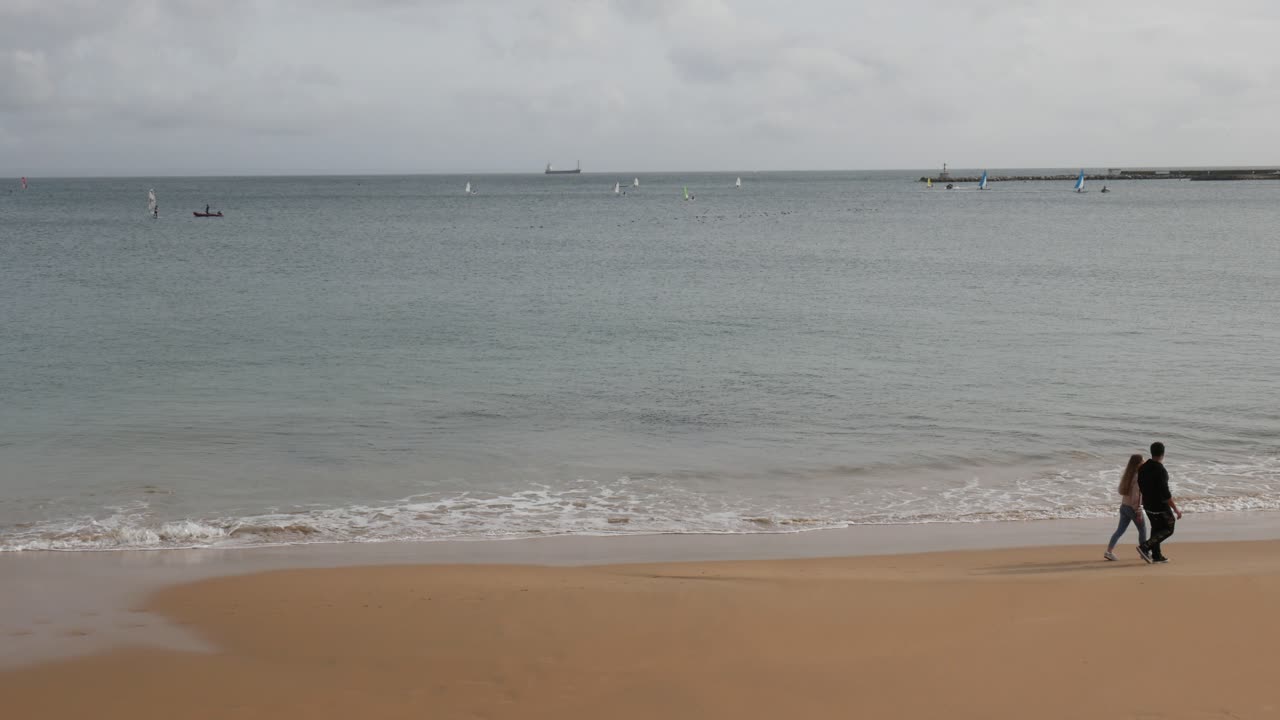 Two people walking from left to right on a beach cloudy day
