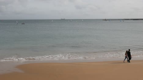 two people walking from left to right on a beach cloudy day