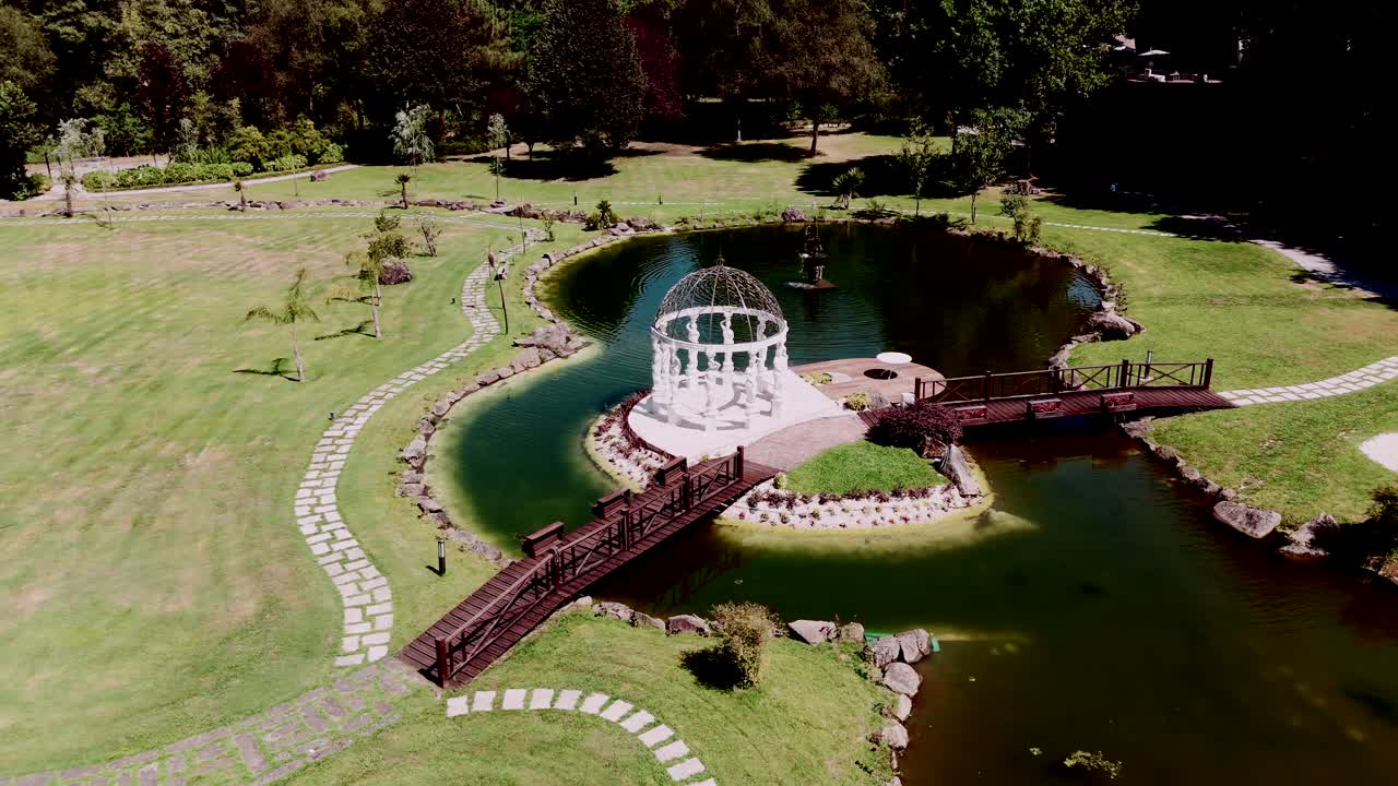 Aerial view of a picturesque lake with a white gazebo and wooden bridge on a manicured lawn