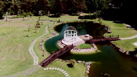 aerial view of a picturesque lake with a white gazebo and wooden bridge on a manicured lawn