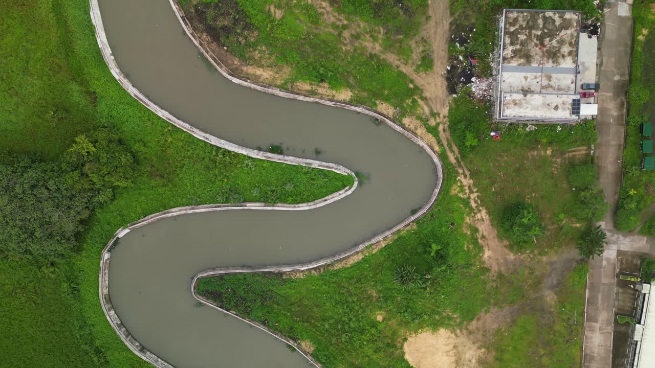 Aerial top-down view of winding river canal amid lush greenery and terrain in Naga City, Bicol, Philippines during daytime