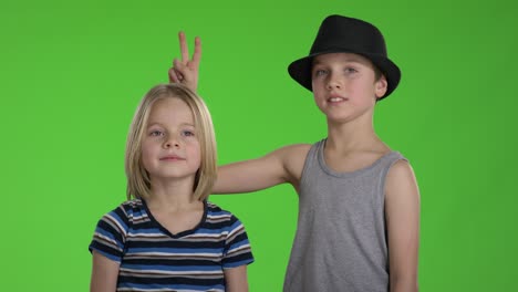 older brother with hat tease younger brother in front of camera while they are posing for a picture