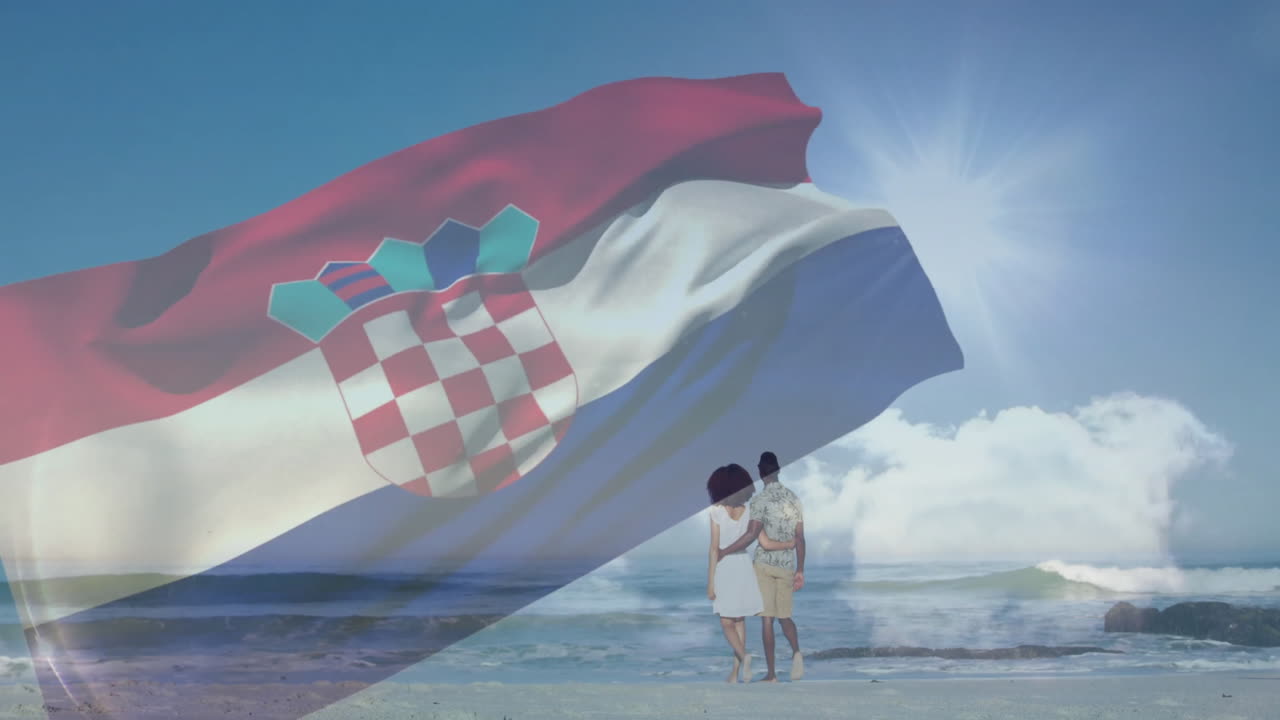 Waving Croatian flag on sunny beach with two people standing nearby