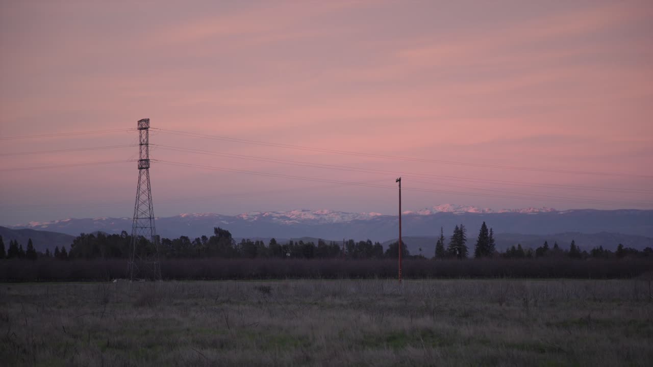 un cielo pastel sobre las montañas de sierra nevada con líneas eléctricas y un campo en primer plano en clovis, ca, ee.uu.