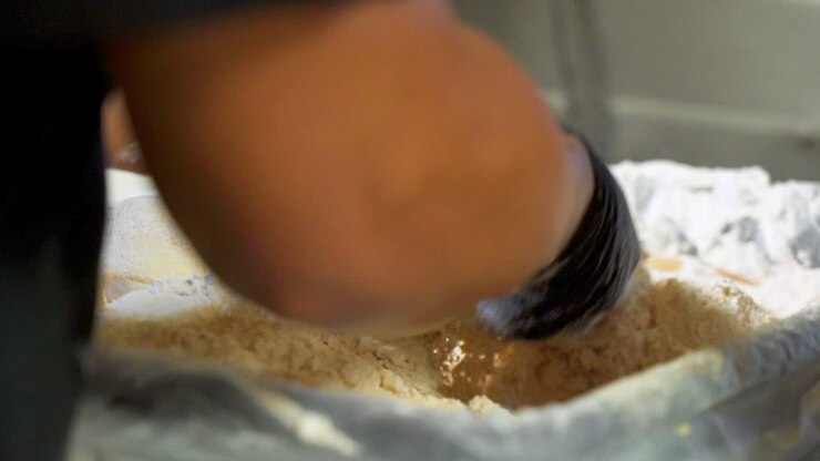 Cook dredges large onion rings in flour, black gloved hands toss onion slices in batter, slider slow motion HD