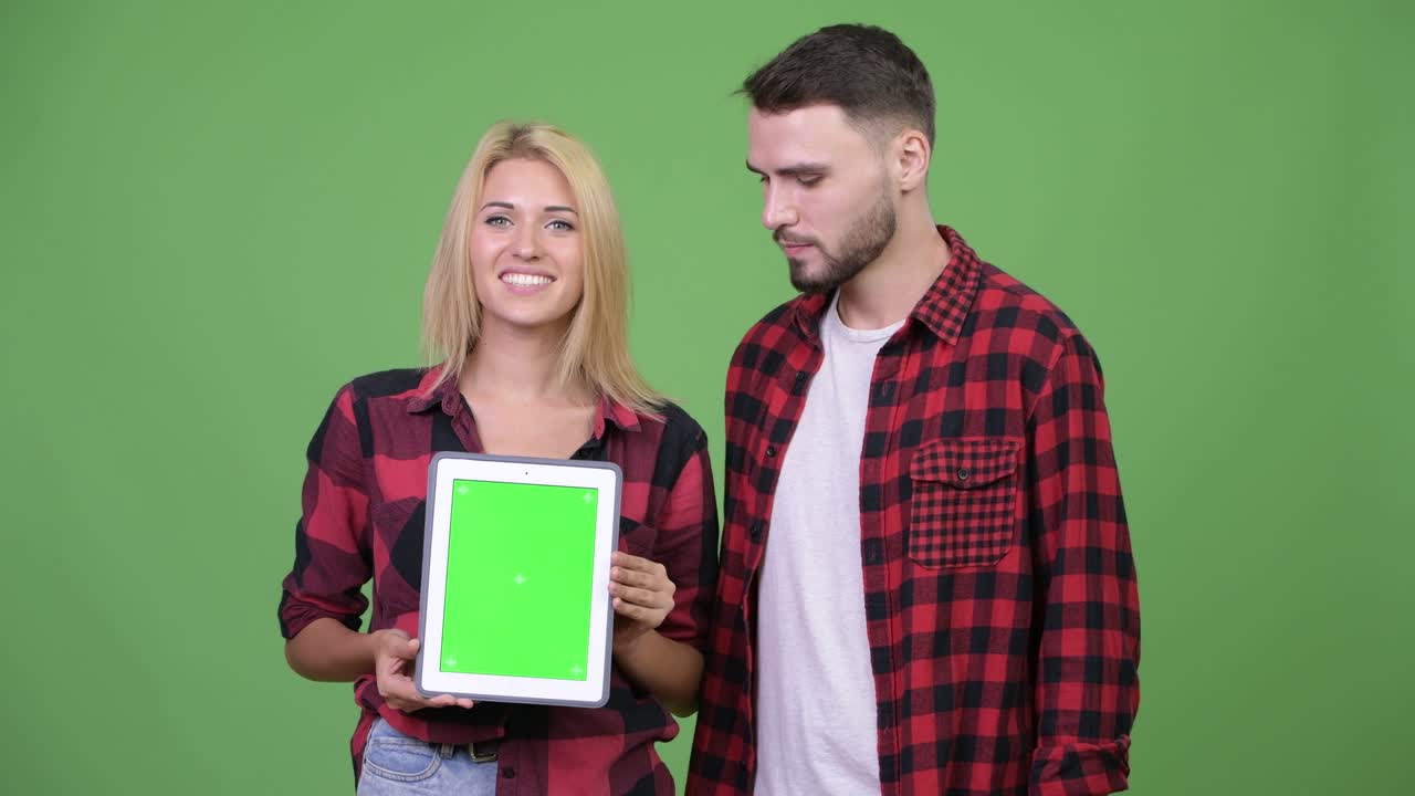 Young couple showing digital tablet together and giving thumbs up