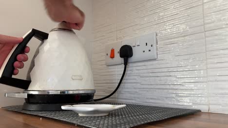 man filling up a white kettle in the kitchen with water to boil to make cup of tea