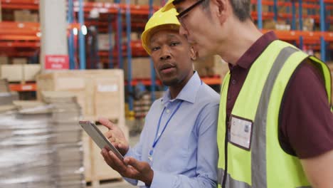 Diverse male workers wearing safety suits and talking in warehouse