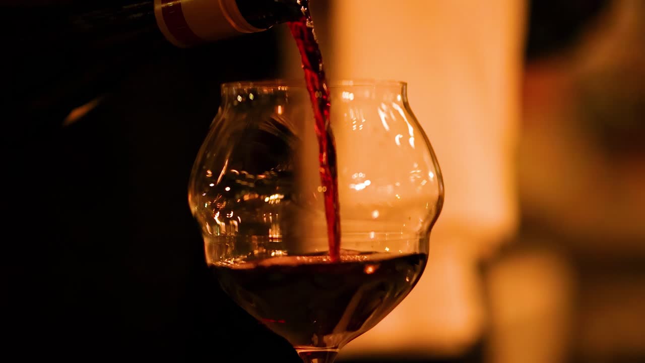 A close-up view of red wine being poured into a glass, highlighting the rich color and texture.
