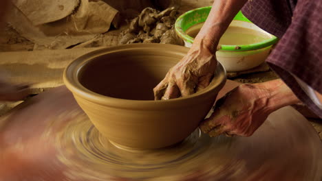 An-Asian-woman-puts-the-final-touch-on-a-new-clay-bowl,-turning-it-on-a-foot-powered-wheel,-showcasing-the-traditional-art-of-pottery-making