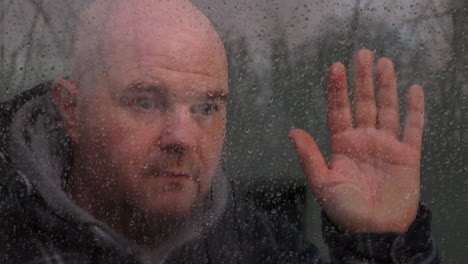 a depressed lonely man feeling isolated looking through a window in the rain