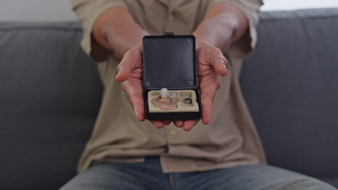 Close up of hands presenting hearing aid device in black box