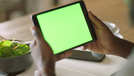 african american man using digital tablet computer watching green screen on mobile device chroma key viewing online entertainment reading social media advertising in cafe close up hands