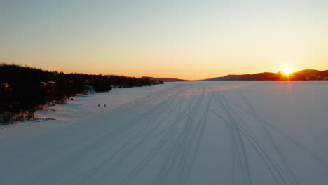 aerial flying over a frozen lake as people play and hike on the ice and snow