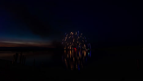 Beautiful-fireworks-reflecting-in-water-of-the-Coquille-River,-Bandon-Oregon,-wood-pilings-in-the-foreground