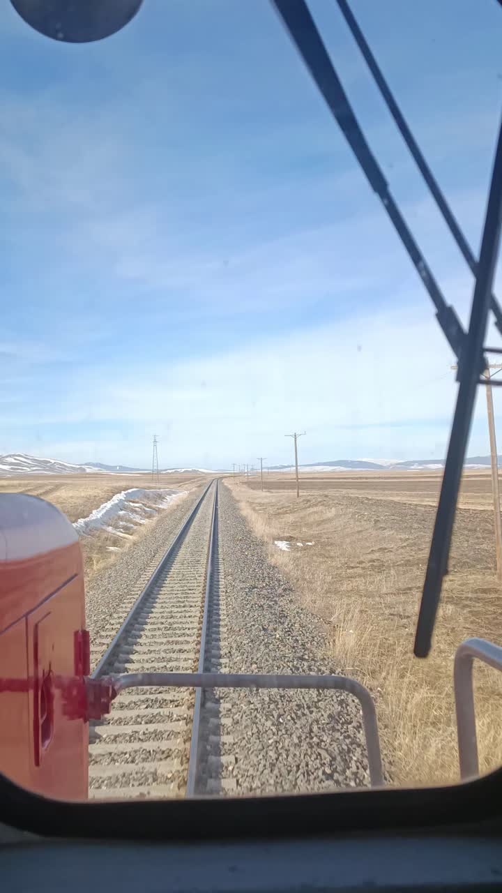 Train operator's view through a window showing railway tracks extending into open fields.