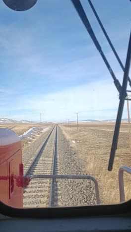 train operator's view through a window showing railway tracks extending into open fields.