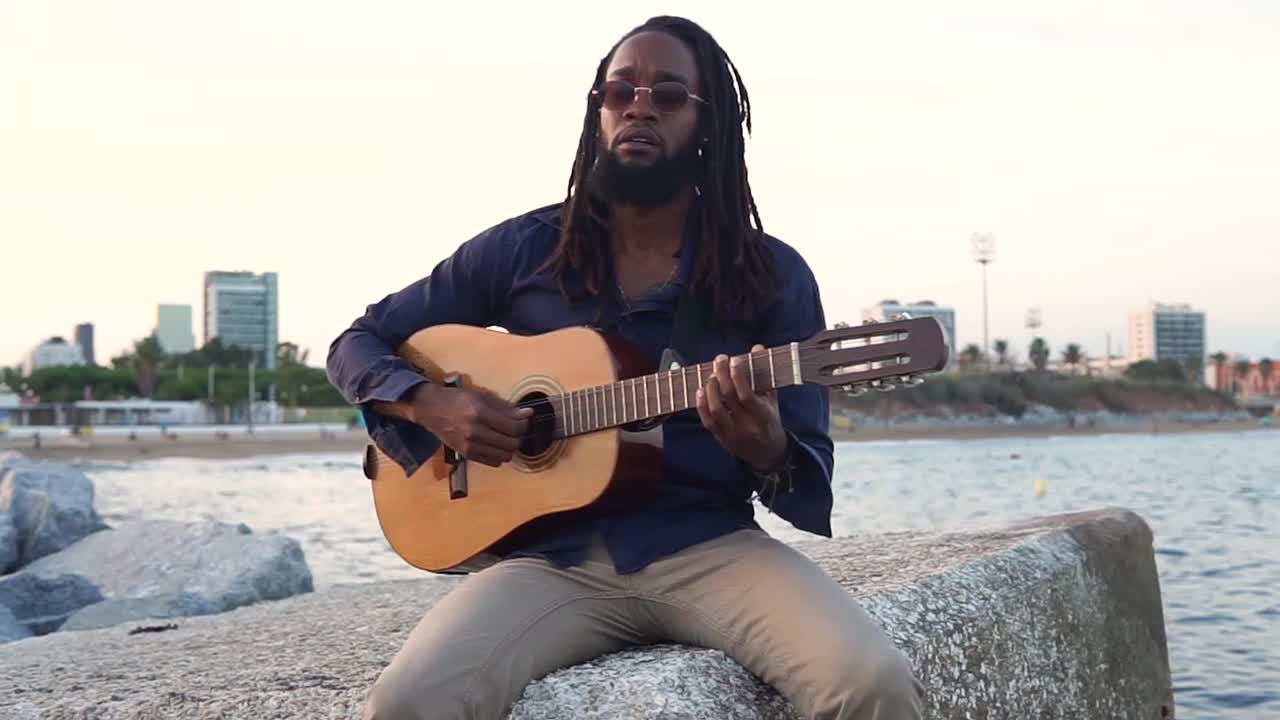 Afroamerikansk musiker spiller guitar ved kysten nær en by