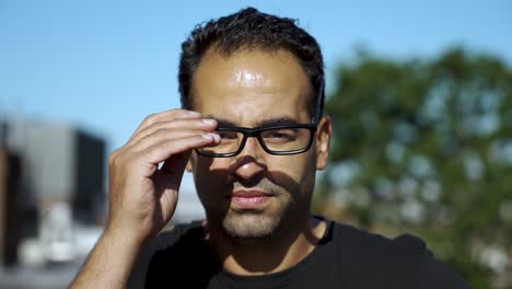 European-athletic-male-putting-on-glasses-on-a-sunny-rooftop,-looking-confident-and-thoughtful