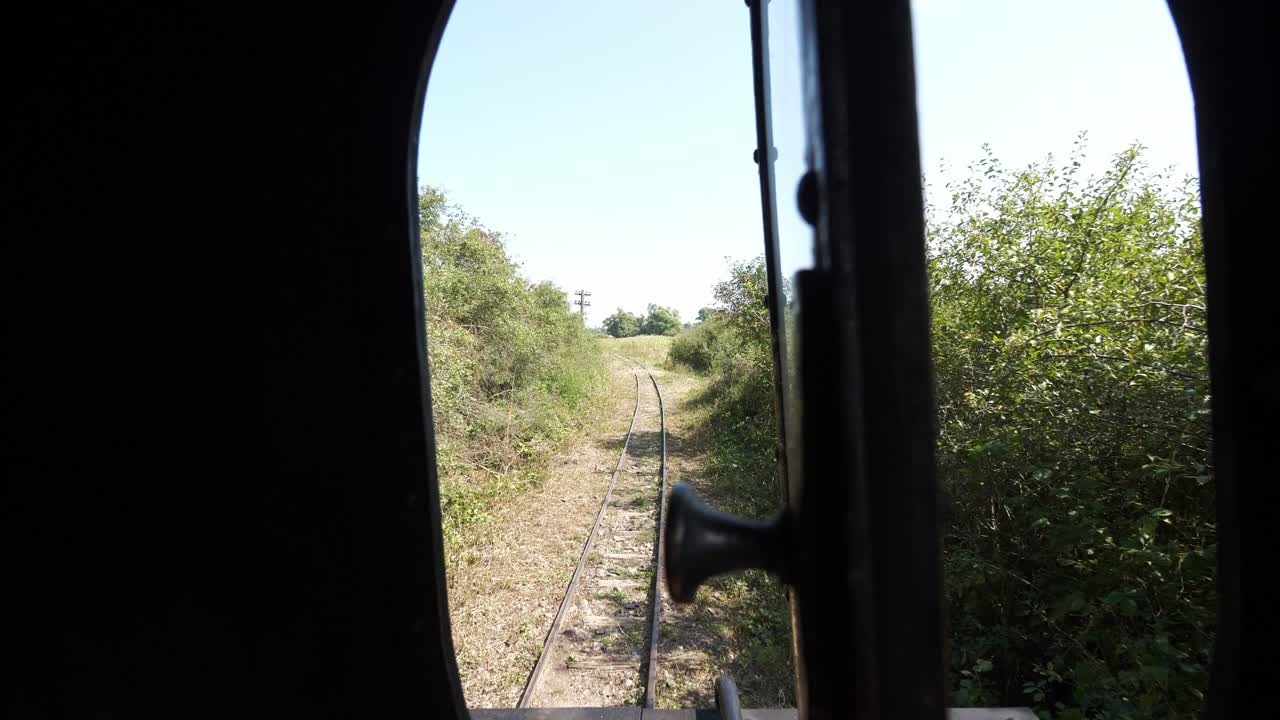 A nostalgic point of view on a journey by vintage train. Looking from an open window, the rural scenery and railway tracks pass by on a sunny summer day, evoking memories of travel