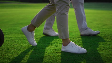 two golfers legs walking on green grass field. golf team carry sport equipment.