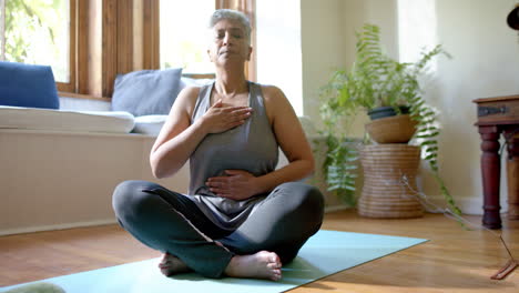 una mujer de dos razas está meditando en una alfombra de yoga en casa.