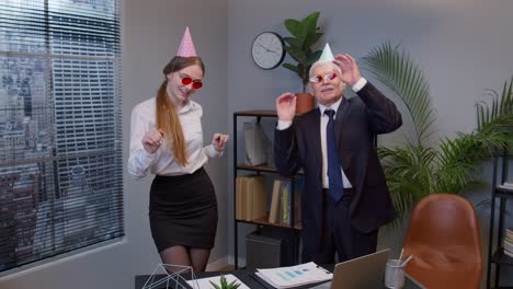 two joyful collegues in formal suits dancing victory dance, celebrating success of business project