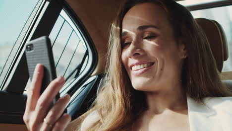 Amigable-Mujer-De-Negocios-Sonriendo-En-Videollamada-En-Un-Teléfono-Inteligente-En-Un-Auto-Moderno-De-Lujo.