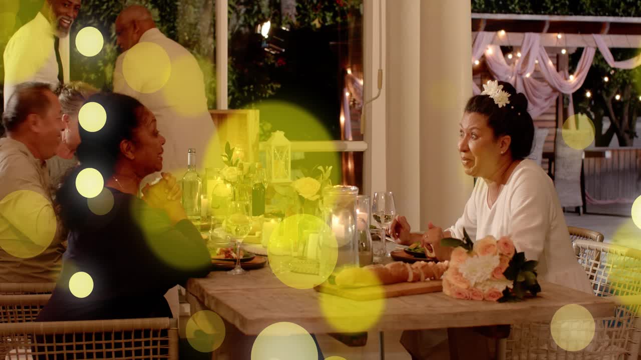 Right woman starting chat urging server moving man rising and guests clapping dinner floating bokeh