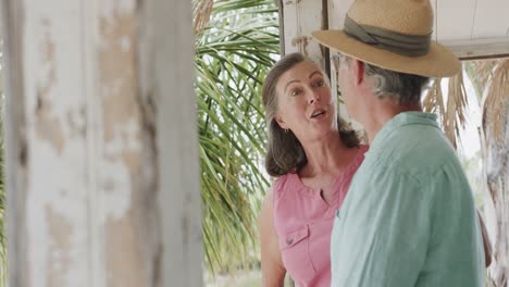 happy senior caucasian couple talking on the porch of wooden beach house, in slow motion