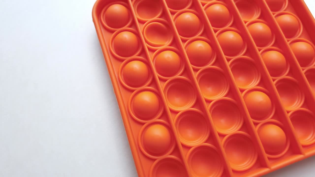 nuevo juguete para bebés. pop it juego de dedos. color gracioso. colorido juego girar en la mesa blanca. cuadrado naranja