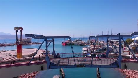 pedestrian bridge leading to a marina with boats and mountains