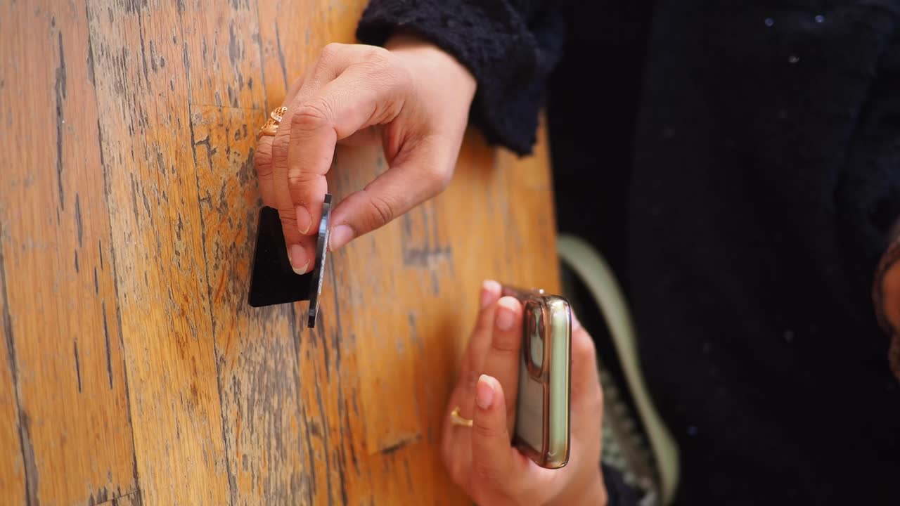 Hands holding a mobile phone and a black object over a wooden table