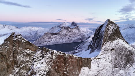 Cinematic aerial view of Segla peak on Senja Island, Norway, steep snow-covered cliffs above icy fjord, dramatic arctic landscape with rugged mountains and winter wilderness
