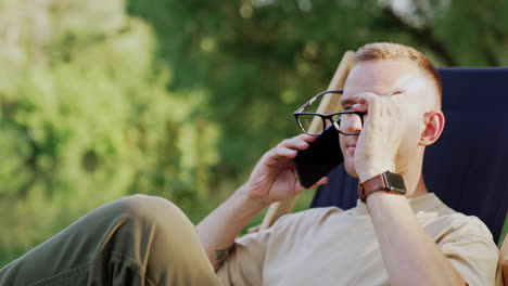 confident male businessman sitting in the chair outdoors. man talks on the phone at backdrop of nature.
