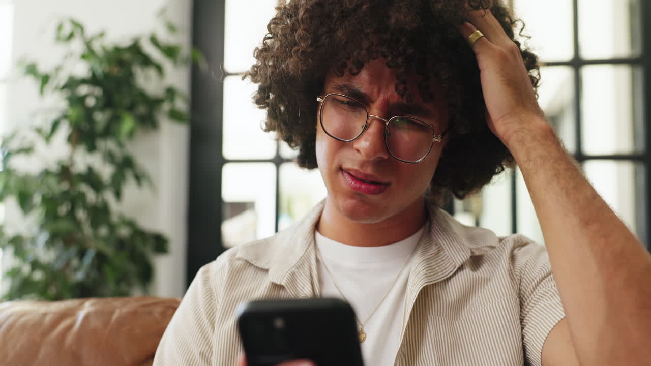 Confused Young Man Looking at Smartphone and Scratching Head