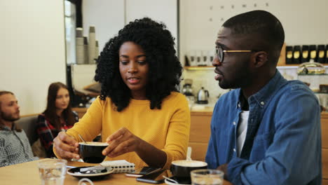 african american man and woman talking and drinking coffee sitting at a table in a cafe