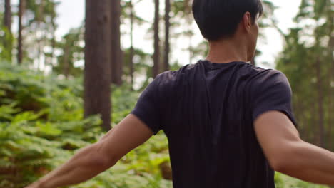 rear view of man warming up and stretching arms before work out exercising running through forest 2