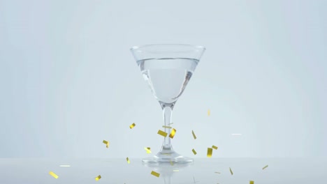 Goldenes-Konfetti-Fällt-über-Oliven,-Die-Vor-Grauem-Hintergrund-In-Ein-Cocktailglas-Fallen