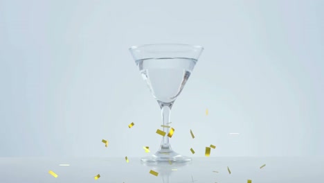 골든 콘페티가 올리브 위로 떨어지고 회색 배경에  ⁇ 테일 잔으로 떨어집니다.