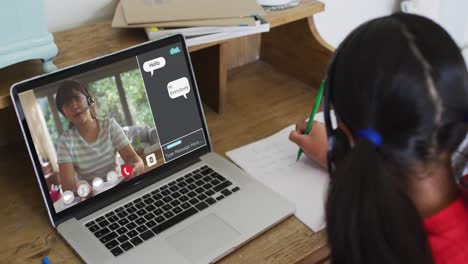 Schoolgirl-using-laptop-for-online-lesson-at-home,-with-her-school-friend-and-web-chat-on-screen