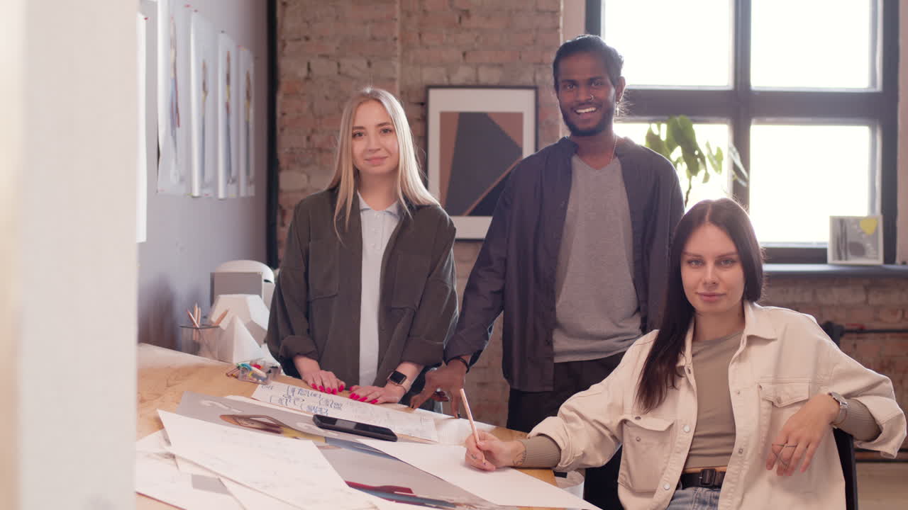 equipo multiétnico de jóvenes diseñadores gráficos mirando y sonriendo a la cámara en un estudio de animación