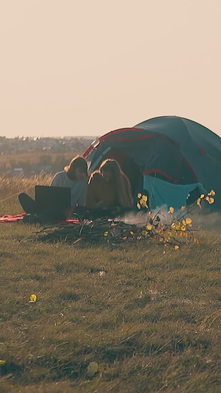 young women tourists with tablet and laptop at tent and bonfire against pictorial autumn river in morning slow motion